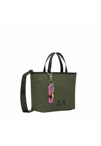 Torba typu tote w oliwkowej zieleni z czarnymi akcentami, wyposażona w zamek błyskawiczny, podwójne uchwyty oraz kolorową breloczek z różnymi kształtami i kolorami.