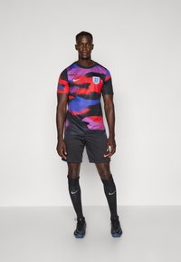 Nike England football kit with a colorful abstract design in black, red, blue, and purple. Includes black shorts, socks, and soccer shoes.