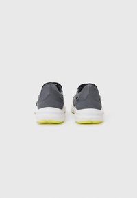 Baskets de sport grises avec un dessus texturé, une semelle intermédiaire blanche et une semelle extérieure verte. Comprend des languettes de traction et un détail de talon renforcé pour le soutien.