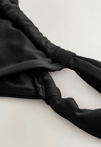 Čierny bikiny korzet s hladkým, elastickým materiálom a zberanými detailmi. Obsahuje nastaviteľné ramienka a uzlový dizajn pre bezpečné nosenie.