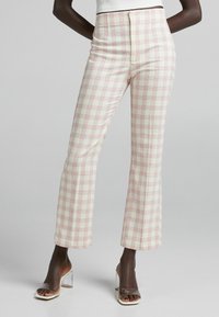 High-waisted plaid trousers in ivory with pink and red checks, tailored fit, and a smooth texture. Paired with clear heeled sandals.