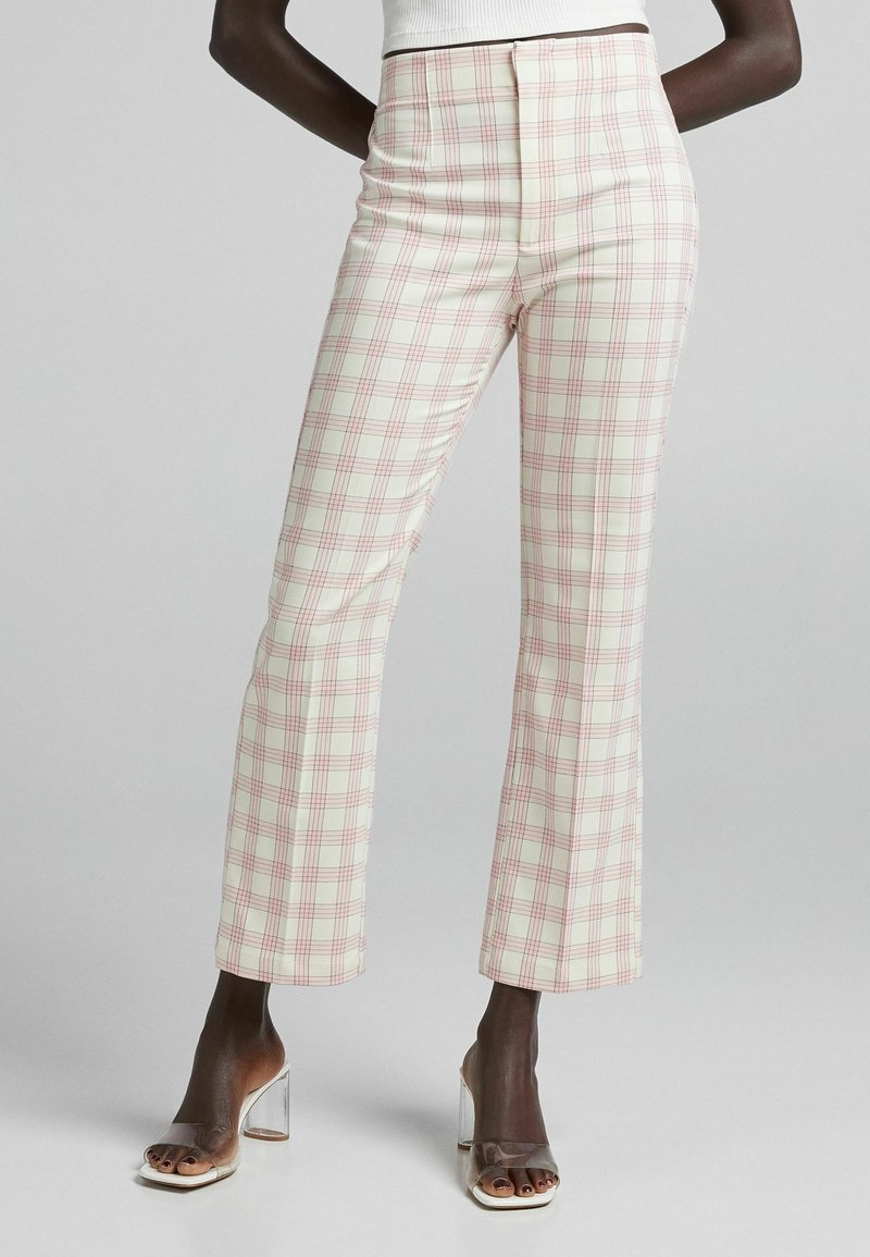 High-waisted plaid trousers in ivory with pink and red checks, tailored fit, and a smooth texture. Paired with clear heeled sandals.