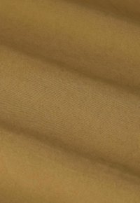 Zacht, gestructureerd materiaal in een warme mosterdkleur met subtiele ribbels, dat een gladde oppervlakte en een lichte glans vertoont.