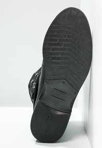 Czarna gumowa podeszwa z bieżnikiem w zygzak, z logo producenta. Gładka faktura z zaokrąglonymi krawędziami i płaskim obcasem.