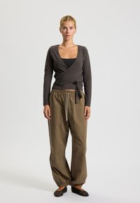 Lonsleeve, ciemnoszara bluzka w stylu wrap, zestawiona z luźnymi, khaki spodniami dresowymi i czarnymi płaskimi butami, z wiązaniem w talii i elastycznymi mankietami.