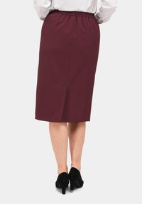 Bordeaux knielange rok met een elastische tailleband, voorzien van een split aan de achterkant voor meer bewegingsvrijheid. Gedragen met zwarte hoge hakken.