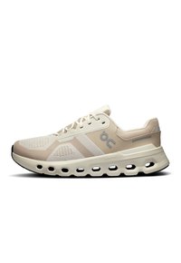Zapatillas deportivas beige con una parte superior de malla transpirable, sutiles acentos blancos y una suela acolchada con recortes distintivos para mayor flexibilidad.