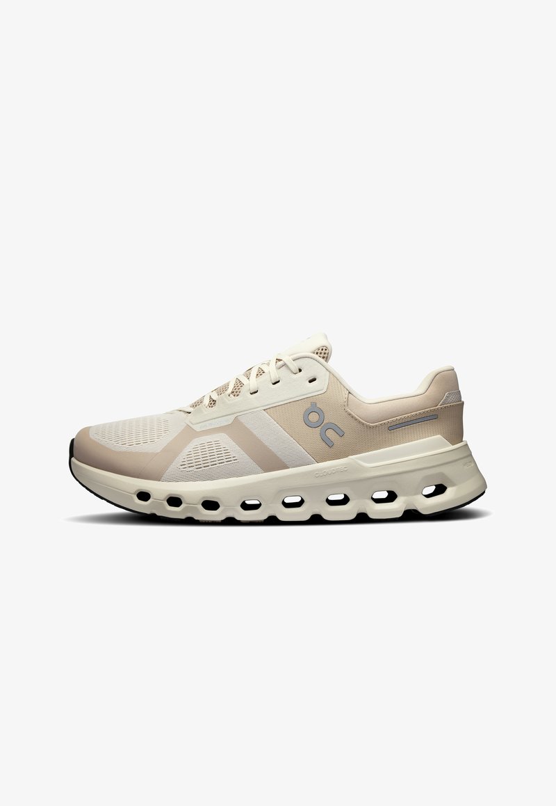 Zapatillas deportivas beige con una parte superior de malla transpirable, sutiles acentos blancos y una suela acolchada con recortes distintivos para mayor flexibilidad.