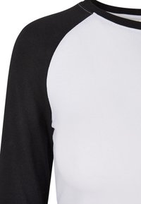 Vit och svart långärmad tröja med raglanärmar, mjukt bomullsmaterial och rundad hals. Kontrastfärgerna skapar en distinkt look.