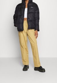 Svart nylon puffjacka med dragkedja och elastiska ärmslut. Kombinerad med beiga cargo-byxor och svarta platåstövlar.