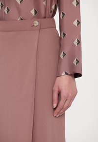 Pikkade varrukatega mauve toonis pluus geomeetrilise mustriga, millele on sobitatud kõrge talje ja ühtlase mauve tooniga seelik, millel on taljes nööbid.