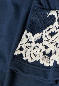 Marineblauwe stof met een textuur van kant in roomkleur met bloemmotief. Vloeiende stof met een zachte afwerking en delicate geborduurde accenten.
