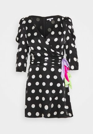 Vestido negro de corte envolvente con grandes lunares blancos, fruncido en la cintura y acentos de cintas coloridas en púrpura, rosa y verde a un lado.
