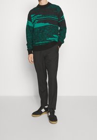 Pull noir et sarcelle à motif avec un col rond, associé à un pantalon habillé noir et des baskets noires avec des accents blancs.