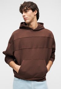 Καφέ φούτερ με κουκούλα και τσέπη, με οριζόντιες ρίγες στο στήθος. Κατασκευασμένο από απαλό ύφασμα με άνετη εφαρμογή.