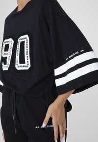 Zwart oversized T-shirt met witte strepen, met een textuur "90" ontwerp versierd met studs. Geaccentueerd met merknaam op de mouw.