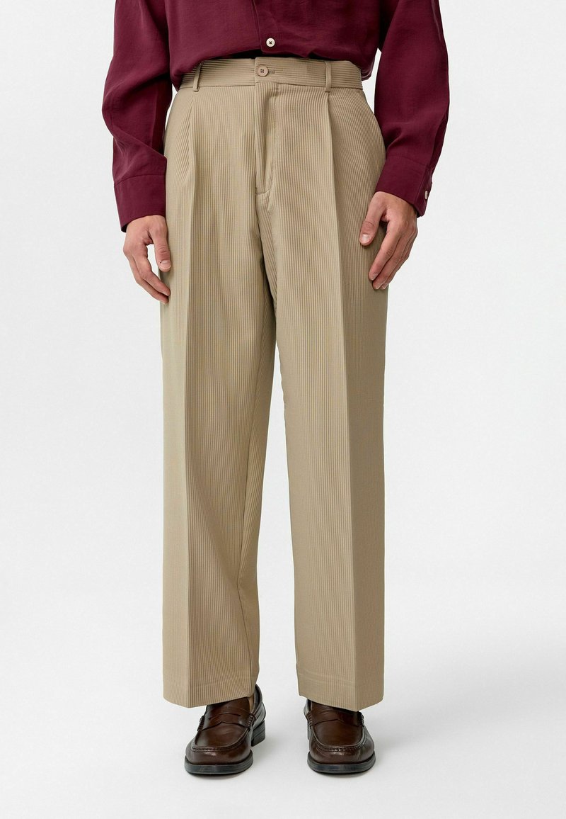 Beige, geplooide broek met een wijdere pijp. Gemaakt van een geweven stof, met een hoge taille en zijzakken. Bruine loafers maken de look compleet.