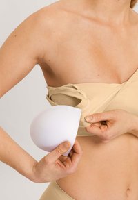 Bralette de tela beige con acolchado de espuma blanca removible. Presenta una textura suave y un diseño ajustable para personalizar.