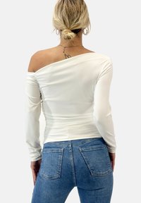 Witte langemende top met een off-shoulder ontwerp, met geplooide textuur. Gecombineerd met blauwe high-waisted jeans met achterzakken.
