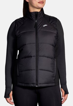 Black puffer vest with a high collar, zip front, and side pockets. Features black long sleeves with thumbholes, made from a lightweight fabric.