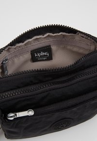 Kipling zwarte ritstas met textuur, meerdere compartimenten en een logo patch aan de binnenkant. De binnenvoering heeft een gladde afwerking.