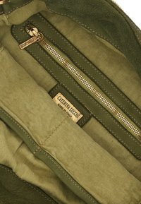 Interno di una borsa di tessuto verde che presenta un compartimento principale, una tasca con zip e un’etichetta con la scritta "Caterina Lucchi, Made in Italy."