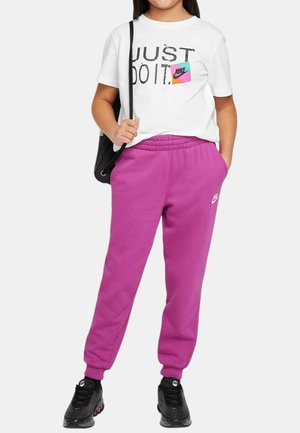 T-shirt bianco con stampa "JUST DO IT" e un logo Nike colorato, abbinato a pantaloni della tuta rosa e scarpe da ginnastica nere.