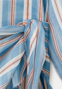 Tissu rayé bleu, blanc et marron noué en un nœud, montrant la texture détaillée et le motif de couleur du tissu.