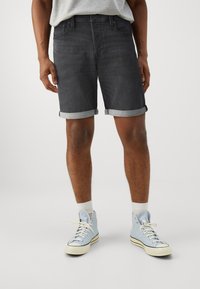Pantalones cortos de mezclilla gris oscuro con dobladillos enrollados, que presentan un diseño clásico de cinco bolsillos. Combinados con zapatillas altas de color azul claro y calcetines blancos.