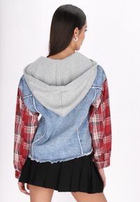 Veste en denim avec capuche grise et manches à carreaux rouges. Présente des bords effilochés et des matériaux contrastants, créant un look superposé. Jupe noire.