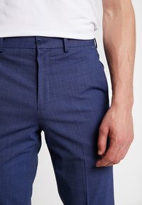 Marinblå skräddarsydda byxor i texturerat tyg, med rak framtill, knappstängning och subtila diagonala linjer i väven.