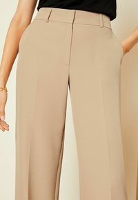 Beige wijde broek van een soepele stof, met een platte voorkant, zijzakken en een getailleerde pasvorm. Geschikt voor casual of formele gelegenheid.