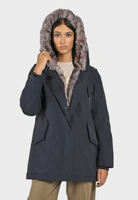 Parka bleu marine avec une capuche à fourrure, fermeture à boutons, grandes poches latérales et une coupe décontractée. Matériau extérieur lisse.