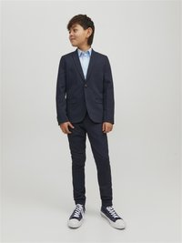 Giacca da uomo blu navy con due bottoni, abbinata a una camicia azzurro chiaro e pantaloni blu navy. Sneakers bianche con dettagli blu completano il look.