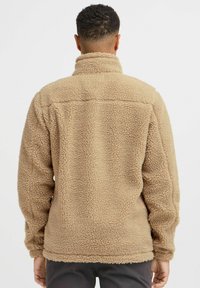 Beige fleece jacket with a textured, soft finish, high collar, and long sleeves, featuring a straight hem and no visible fastenings.