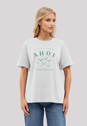 White cotton t-shirt with a loose fit. Front features green text and bird illustrations. Round neck and short sleeves. Worn with blue jeans.