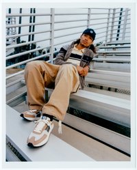 Ljusbruna och vita sneakers med svarta accenter, mjukt tyg, breda beige byxor och en grå zip-up-jacka över en randig tröja.