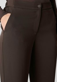 Pantaloni marroni su misura con chiusura a zip e bottone, dotati di tasche laterali e un tessuto liscio e strutturato.