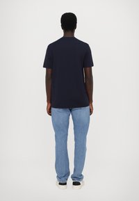 Jūrinė trumpomis rankovėmis marškinėliai, pagaminti iš medvilnės, laisvas pritaikymas, derinami su šviesiai mėlynomis džinsų kelnėmis, balti sportbačiai su juodais akcentais.