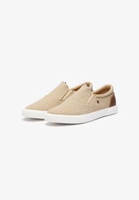 Beige instapschoenen van canvas met een witte rubberen zool. Bruine suède accenten op de hiel. Elastische zijpanelen en gestikte details.