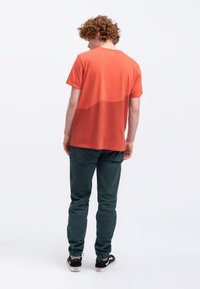 Heren oranje T-shirt met een gradient ontwerp dat overgaat in een donkerdere tint bij de zoom. Gepaard met groene broek en zwarte sneakers.
