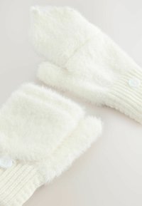 Een paar witte, fuzzy gebreide omvormbare wanten met een knoopflap, plat gelegd op een lichte ondergrond.