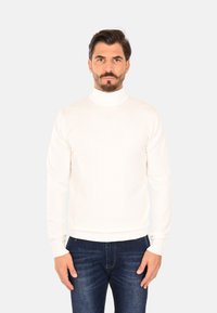 Maglione dolcevita bianco realizzato in tessuto morbido, con maniche lunghe e silhouette aderente. Abbinato a jeans blu scuro, vista frontale.
