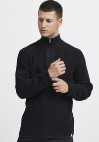 Schwarzer Reißverschluss-Pullover mit einem strukturierten, gerippten Muster. Verfügt über lange Ärmel und einen hohen Kragen mit einem silbernen Reißverschluss. Lässiger Schnitt.