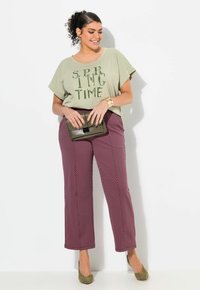 Lichtgroene katoen t-shirt met "SPRING TIME" in sequins letters, gecombineerd met wijdvallende kastanjebruine broek met een stippenpatroon en olijfgroene hakken.