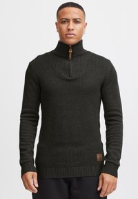Dark green knit sweater featuring a high collar with a half-zip, ribbed cuffs and hem, and a small branded leather patch on the side.