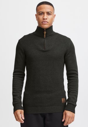 Dark green knit sweater featuring a high collar with a half-zip, ribbed cuffs and hem, and a small branded leather patch on the side.