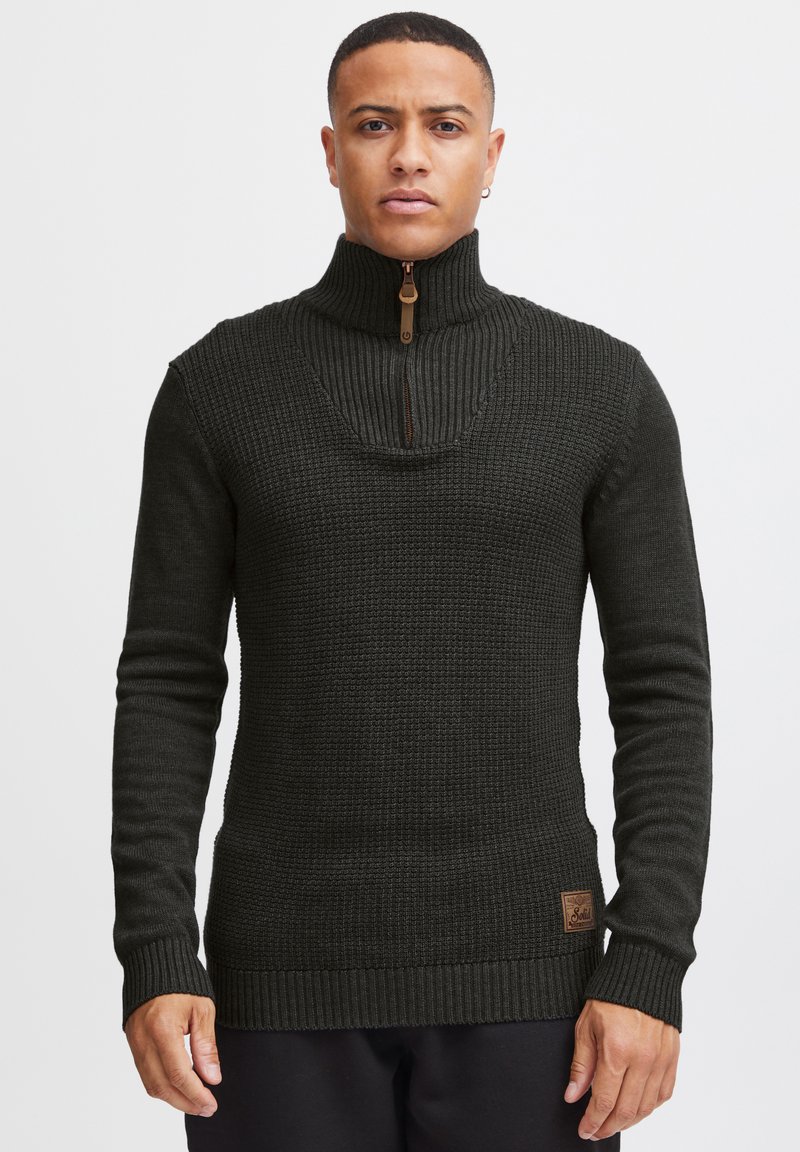 Dark green knit sweater featuring a high collar with a half-zip, ribbed cuffs and hem, and a small branded leather patch on the side.