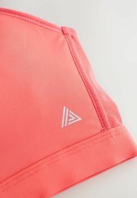 Prim-plan cu țesătură de sutien sport coral roz, cu cusături cusute și logo geometric alb mic pe o suprafață netedă.