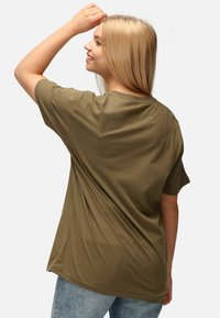 Camiseta de algodón de corte corto en color verde oliva, con un ajuste holgado y un escote redondo, combinada con unos vaqueros de lavado claro.